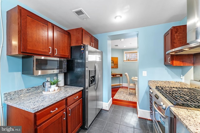 kitchen featuring light stone counters, dark tile patterned flooring, appliances with stainless steel finishes, and wall chimney exhaust hood