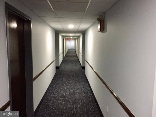 hallway featuring a paneled ceiling and dark colored carpet