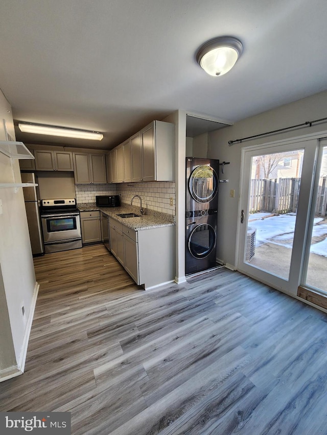 kitchen with sink, stacked washing maching and dryer, gray cabinetry, stainless steel appliances, and light stone counters