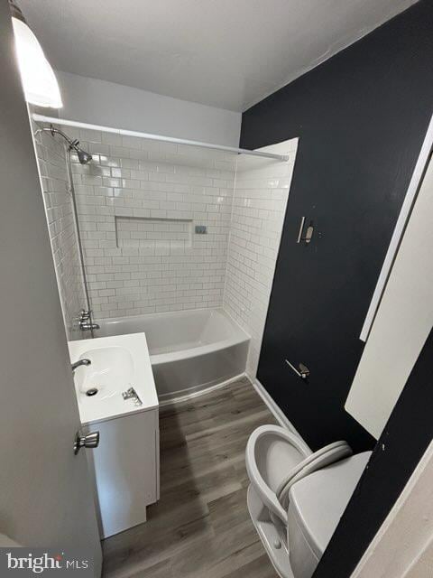 full bathroom with tiled shower / bath combo, vanity, hardwood / wood-style floors, and toilet