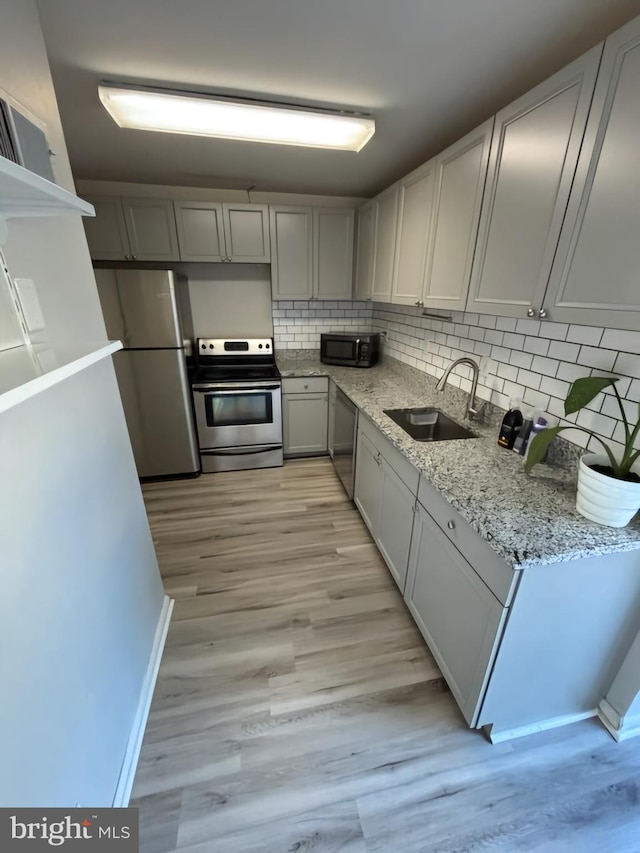 kitchen featuring tasteful backsplash, sink, light stone counters, light hardwood / wood-style floors, and stainless steel appliances