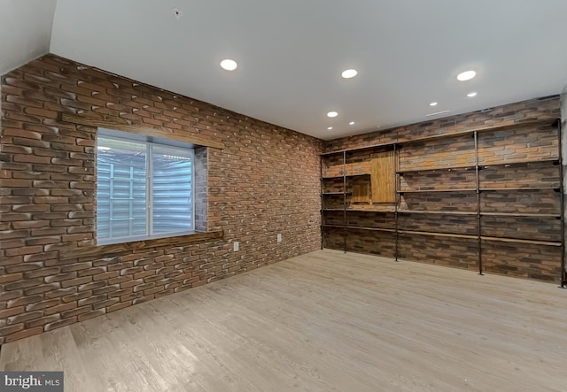 spare room featuring brick wall and light hardwood / wood-style floors