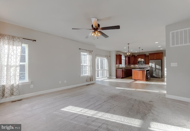 unfurnished living room with ceiling fan, light colored carpet, and a wealth of natural light