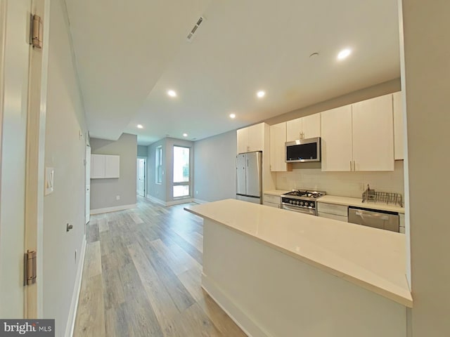 kitchen featuring white cabinets, decorative backsplash, stainless steel appliances, and light hardwood / wood-style floors