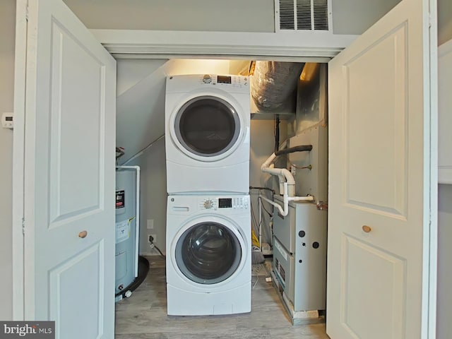 laundry room featuring stacked washer / drying machine, water heater, and light hardwood / wood-style floors