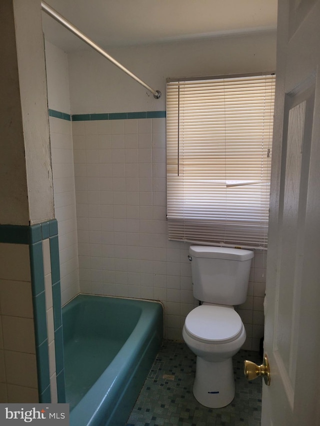 bathroom with toilet, tile patterned floors, and tile walls