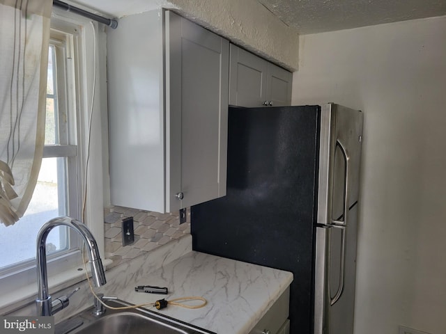 kitchen with light stone countertops, a textured ceiling, decorative backsplash, sink, and stainless steel fridge