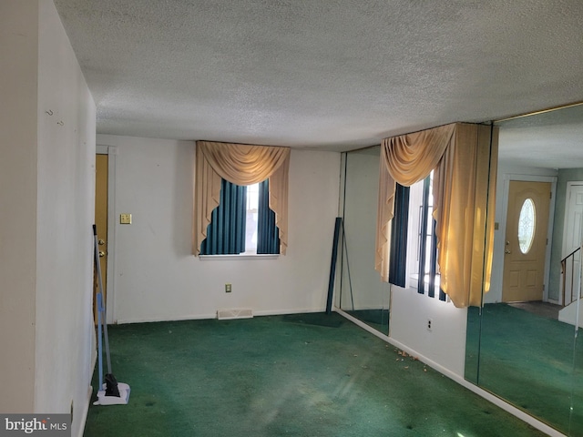 unfurnished room with a healthy amount of sunlight, dark colored carpet, and a textured ceiling