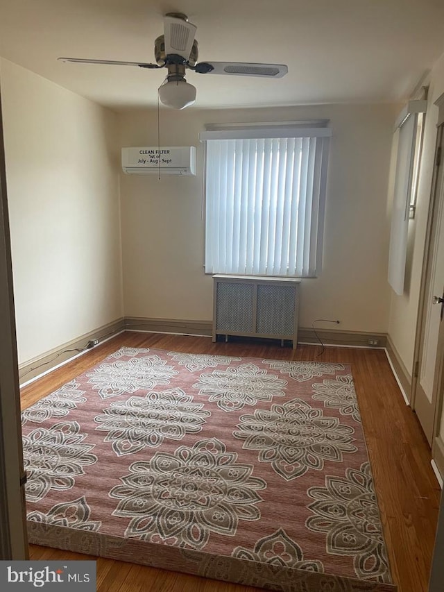 unfurnished room featuring ceiling fan, radiator heating unit, an AC wall unit, and wood-type flooring