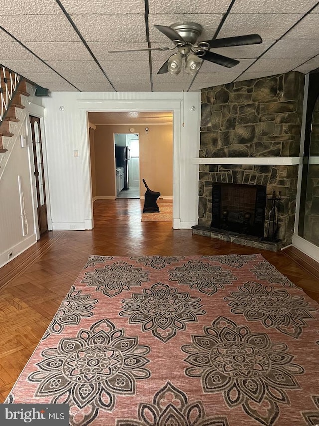 living room featuring hardwood / wood-style flooring, a stone fireplace, a paneled ceiling, and ceiling fan