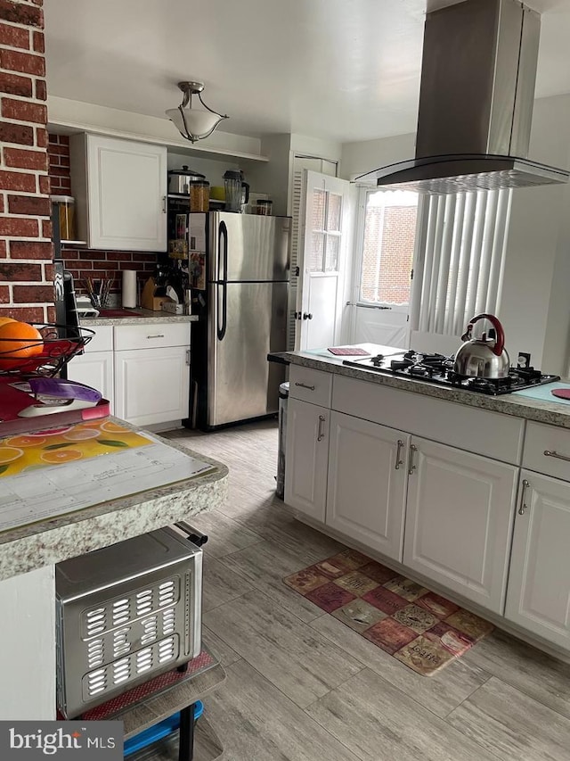 kitchen with stainless steel fridge, gas cooktop, white cabinets, and island exhaust hood