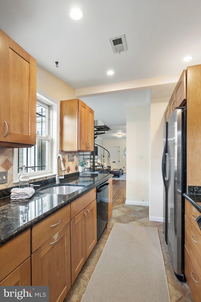 kitchen with sink, stainless steel refrigerator, black dishwasher, dark stone counters, and decorative backsplash