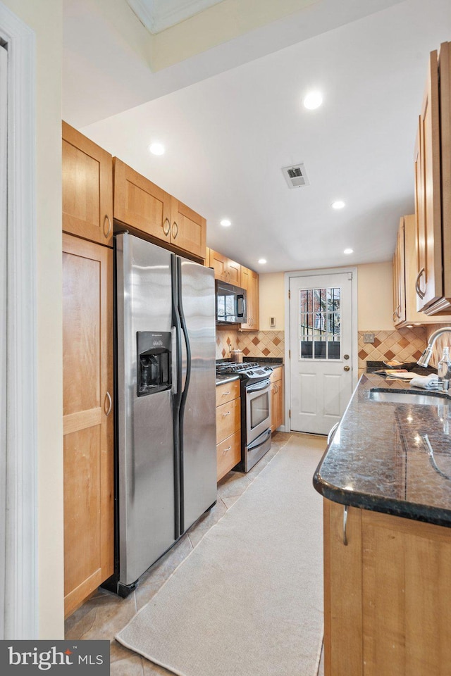 kitchen with stainless steel appliances, sink, decorative backsplash, and dark stone countertops