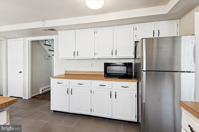 kitchen with white cabinets, a baseboard radiator, freestanding refrigerator, black microwave, and wooden counters