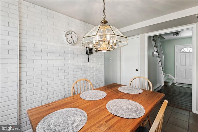 dining room featuring a baseboard radiator, brick wall, dark tile patterned floors, and stairs