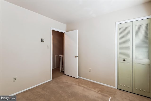 unfurnished bedroom featuring light carpet, a closet, and baseboards