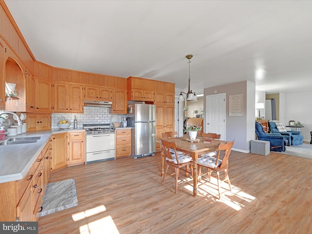 kitchen featuring pendant lighting, gas range gas stove, sink, stainless steel fridge, and light wood-type flooring