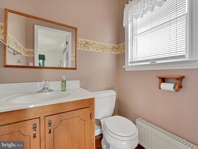 bathroom featuring toilet, radiator heating unit, vanity, and a healthy amount of sunlight