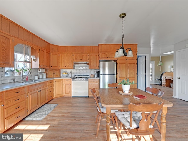 kitchen with decorative light fixtures, white range with gas cooktop, decorative backsplash, sink, and stainless steel refrigerator