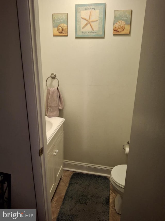 half bathroom featuring toilet, tile patterned flooring, vanity, and baseboards