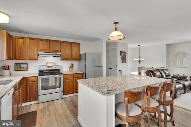 kitchen with a kitchen bar, appliances with stainless steel finishes, pendant lighting, light stone countertops, and light hardwood / wood-style floors