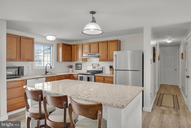 kitchen with sink, decorative light fixtures, light hardwood / wood-style flooring, appliances with stainless steel finishes, and a kitchen island