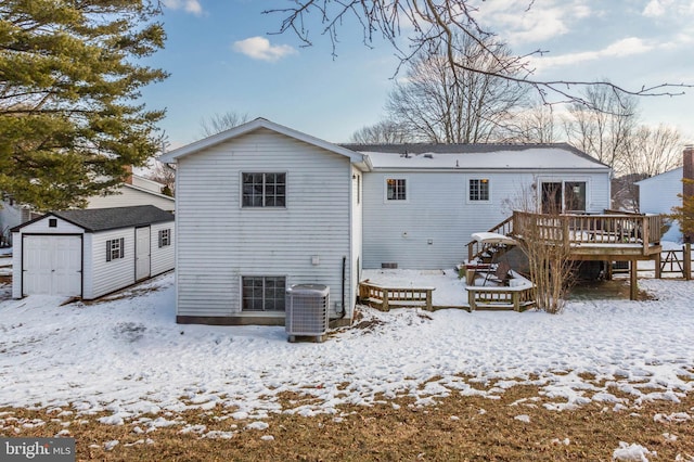 snow covered rear of property featuring a wooden deck, central AC, and a storage shed