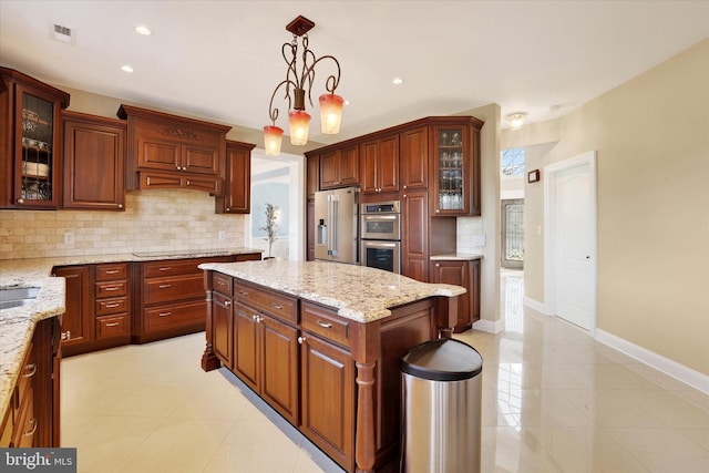 kitchen featuring appliances with stainless steel finishes, decorative light fixtures, backsplash, light stone counters, and a center island