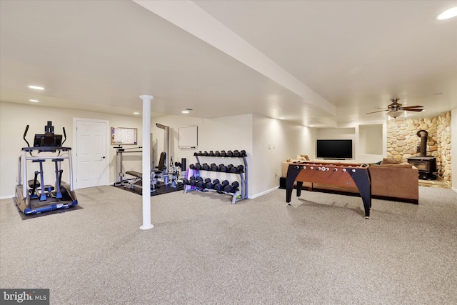 exercise room with a wood stove, ceiling fan, and carpet floors