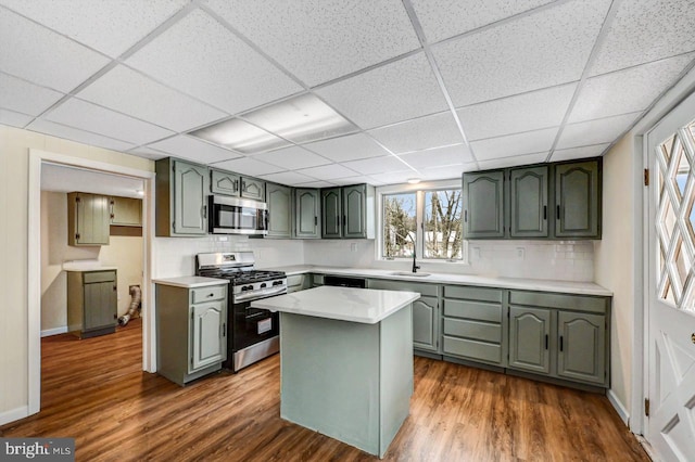 kitchen with dark wood-type flooring, a paneled ceiling, green cabinetry, decorative backsplash, and stainless steel appliances