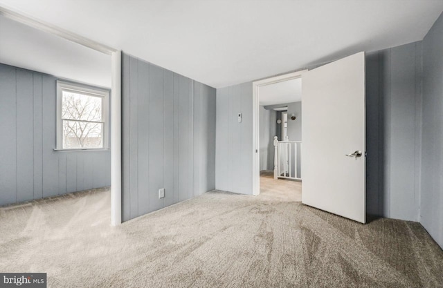 empty room featuring light colored carpet and wooden walls