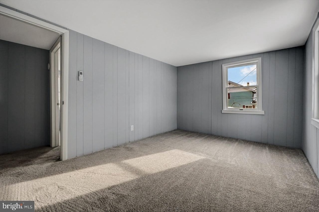 carpeted empty room featuring wooden walls