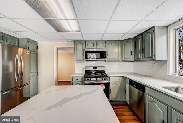 kitchen featuring stainless steel appliances, green cabinets, light stone countertops, and a drop ceiling