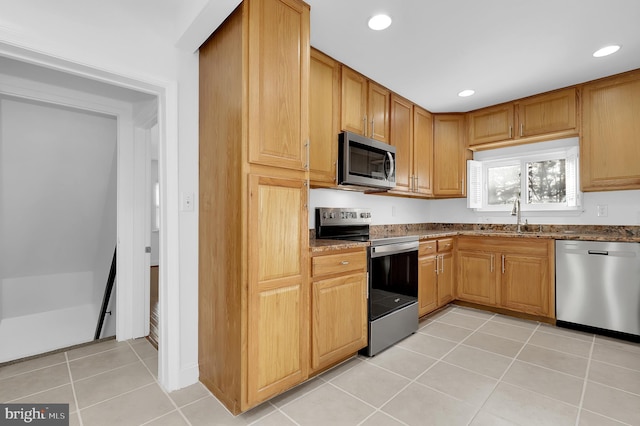 kitchen featuring stainless steel appliances, sink, dark stone counters, and light tile patterned floors