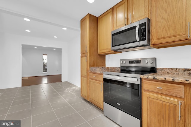 kitchen with appliances with stainless steel finishes, light tile patterned floors, and light stone counters