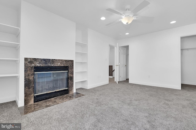 unfurnished living room featuring ceiling fan, carpet flooring, a fireplace, and built in shelves