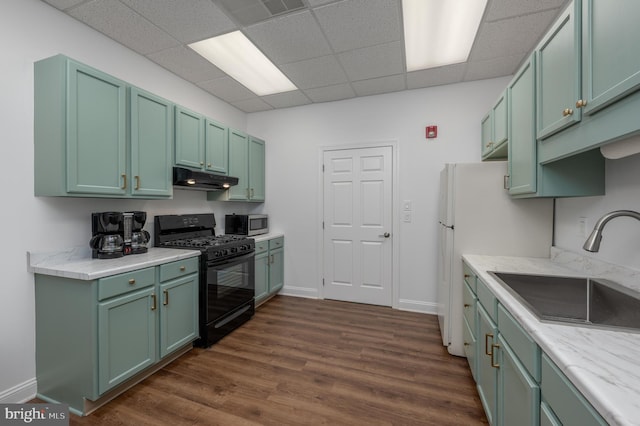 kitchen with black gas range oven, sink, dark hardwood / wood-style floors, green cabinetry, and a drop ceiling