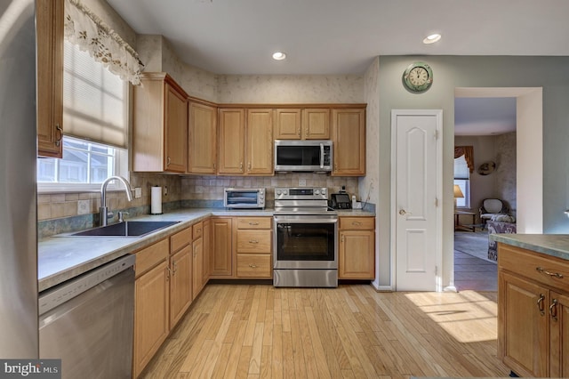 kitchen featuring sink, light hardwood / wood-style floors, decorative backsplash, and stainless steel appliances