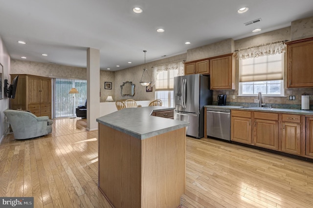 kitchen featuring a kitchen island, stainless steel appliances, light hardwood / wood-style floors, sink, and hanging light fixtures