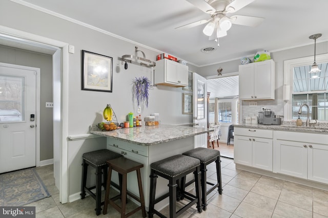 kitchen featuring a breakfast bar area, light stone countertops, sink, and white cabinetry