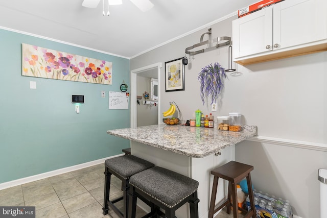 kitchen featuring light tile patterned floors, white cabinetry, a breakfast bar area, light stone countertops, and crown molding