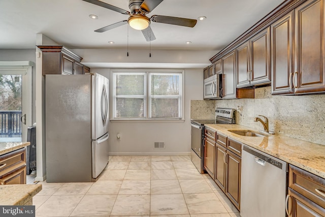 kitchen with appliances with stainless steel finishes, decorative backsplash, sink, light stone counters, and light tile patterned flooring