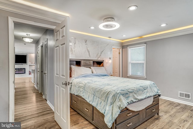 bedroom featuring light wood-type flooring, a stone fireplace, and crown molding