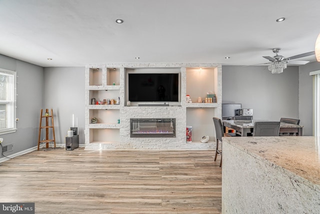 living room featuring light hardwood / wood-style floors, built in features, a stone fireplace, and ceiling fan