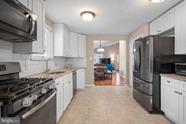 kitchen with stainless steel appliances, white cabinetry, light stone countertops, and sink