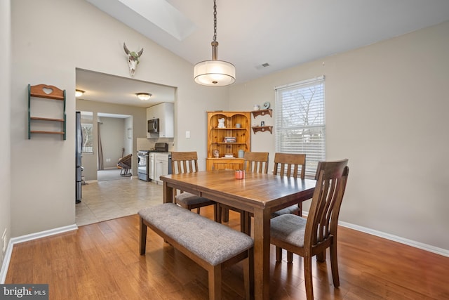 dining room featuring vaulted ceiling with skylight and light hardwood / wood-style floors