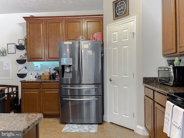 kitchen featuring light tile patterned flooring, dark stone counters, stainless steel fridge with ice dispenser, and a textured ceiling