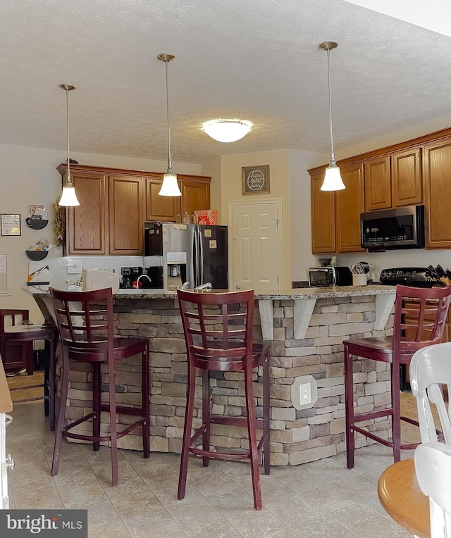 kitchen with pendant lighting, a breakfast bar area, appliances with stainless steel finishes, light stone countertops, and a textured ceiling