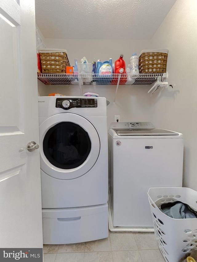 clothes washing area with light tile patterned flooring, separate washer and dryer, and a textured ceiling