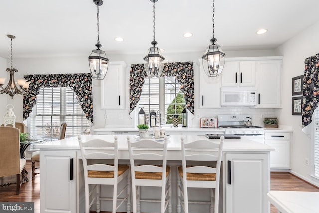 kitchen with white appliances, a chandelier, white cabinets, decorative light fixtures, and a center island with sink